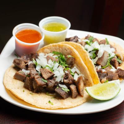 Beef tongue tacos with chopped onions and cilantro served with salsas and lime.