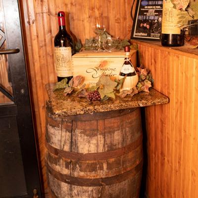 Two wine bottles, wine box, and glasses for wine displayed on a rustic barrel inside.