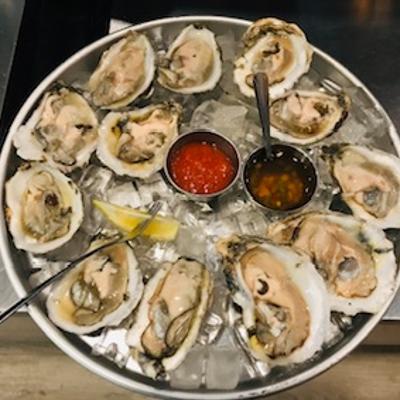 Fresh raw oysters served on a bed of ice with two sauces and a lemon wedge.