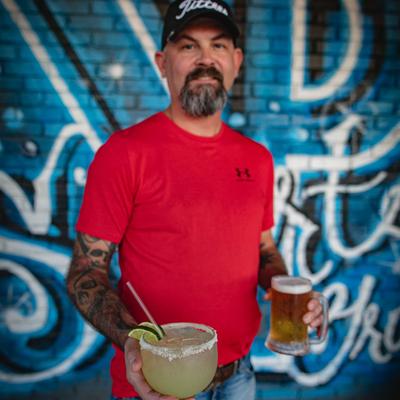 A person standing in front of a graffiti wall  holding a margarita and beer.