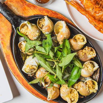 A sizzling cast-iron skillet of sea snails, garnished with fresh herbs.