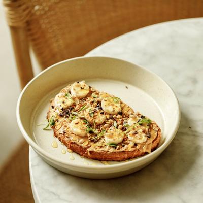 Banana topped toast with nuts on a beige plate.