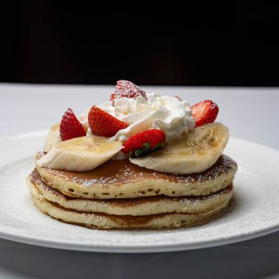 Pancakes topped with whipped cream, sliced bananas, and strawberries.