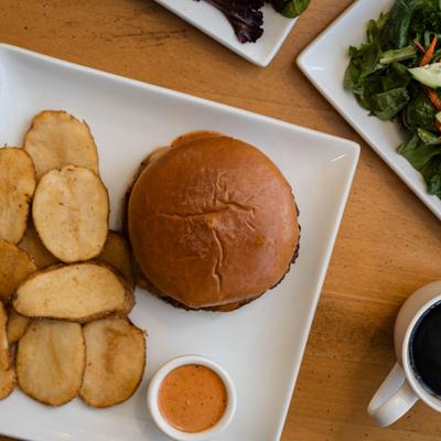Overhead view of a burger with a side of potato chips and dipping sauce.