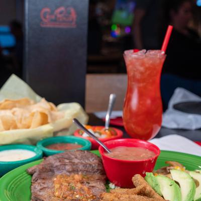 Bistek a La Mexicana plate, accompanied with chips, dipping, salad, and a red cocktail.