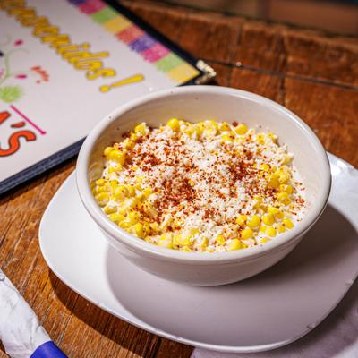 Bowl of Elote featuring corn kernels mixed with mayo, topped with cheese and chili powder.