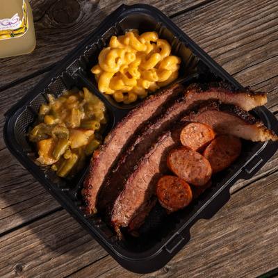 Brisket, sausage, macaroni and cheese, and green beans in a takeout tray.