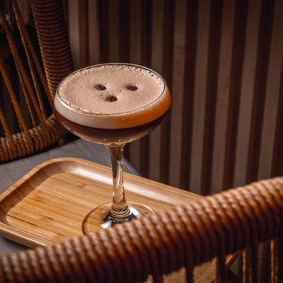 Foamy Espresso Martini cocktail with coffee beans on wooden tray.