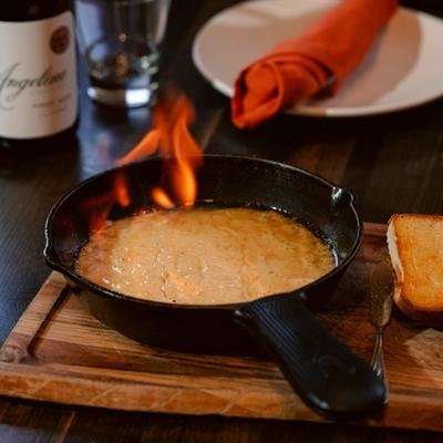 Saganaki cheese being flambéed in a pan on the table.