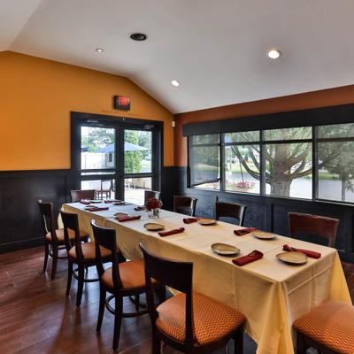 Interior,  a long, set table with dark wooden chairs, orange accent walls, and large windows.
