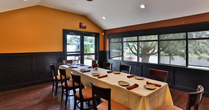 Dining room with a long table set for a meal, surrounded by chairs, windows on one side