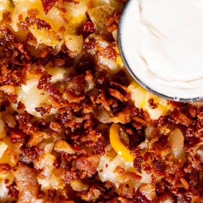 Close up of loaded smashed potato and a side of sour cream.