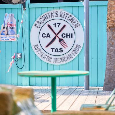 Restaurant sign on a turquoise patio wall near a fountain.