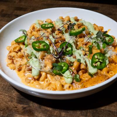 Macaroni and cheese topped with sliced fresh jalapeños and a drizzle of green sauce.
