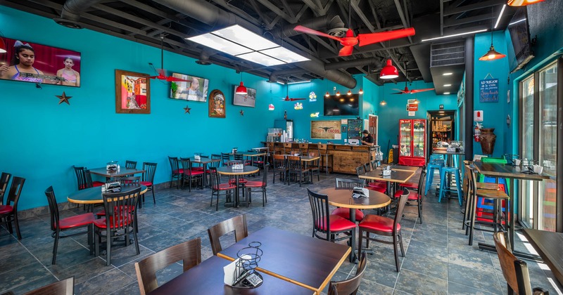 Interior, seating area, tables with chairs, bar with stools in the back, TVs on the wall