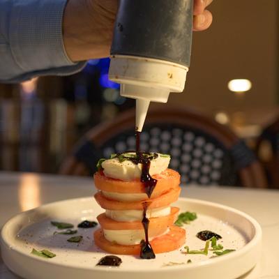 A freshly prepared Caprese salad being drizzled with a balsamic reduction.