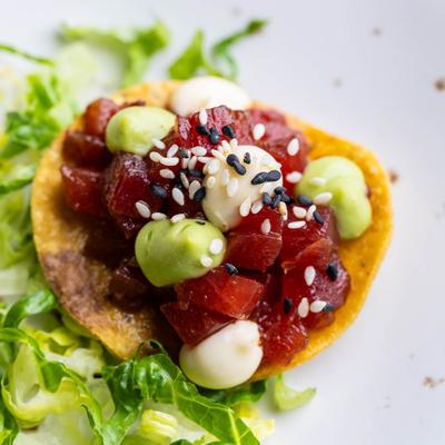Tuna tostada topped with sesame seeds, mayo, and avocado sauce.