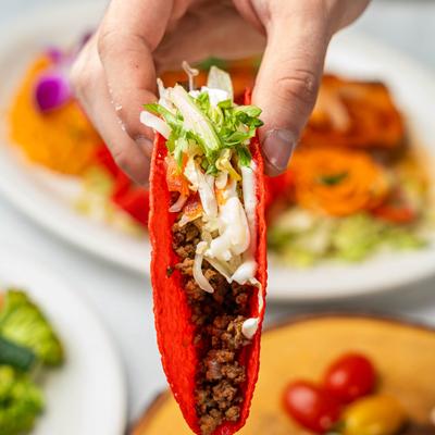 Beef taco in hand with blurred food in the background.