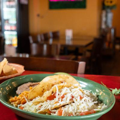 Two beef tacos topped with cheese and tomatoes, served with rice and refried beans.