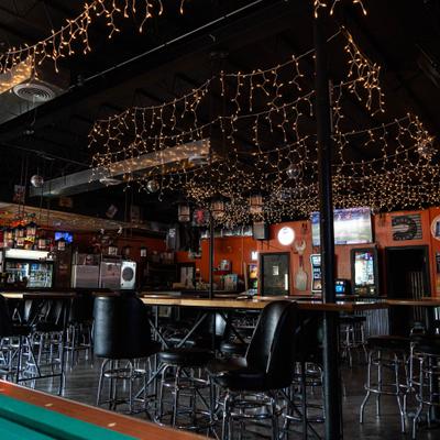 Bar interior with a pool table, high-top seating, and string lights.