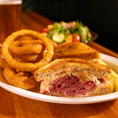 Reuben sandwich served with a side of onion rings.