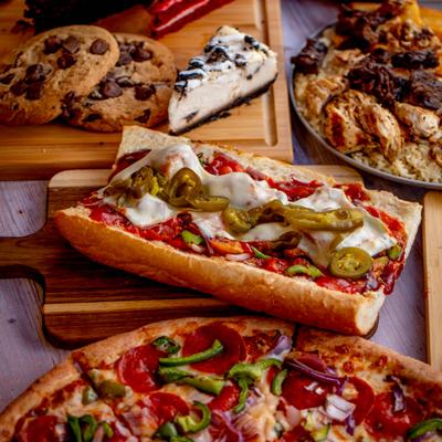 Sandwich served on the wooden board alongside a pizza and desserts.