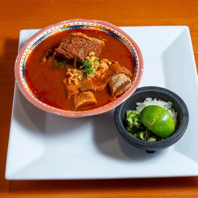Mexican beef and vegetable soup with a side dish of onions, jalapenos and a lime wedge.