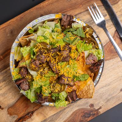 Bowl of nachos topped with steak, lettuce and cheese.