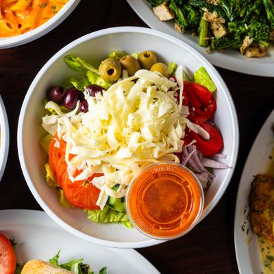 Greek salad topped with greted cheese and served with a dressing cup.