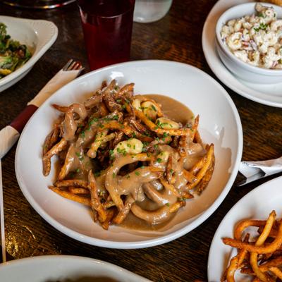 Poutine plate served on a wooden table with surrounding food plates and drinks.