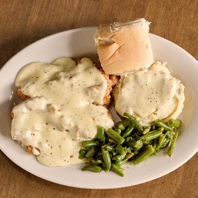 Country fried chicken topped with gravy, served with mashed potato, green beans and a bread roll.
