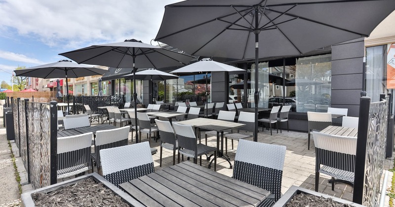 Exterior, partially covered seating area, parasols, plastic wicker chairs, abstract metal fence