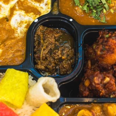 Indian meal tray with curries, fried snacks, rice, and vegetable sides.