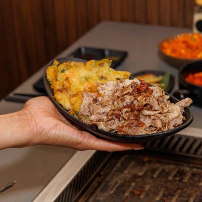 A hand holding a plate of thinly sliced beef and seafood pancakes.