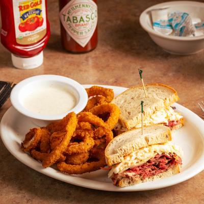 Pastrami sandwich with onion rings and dipping sauce.
