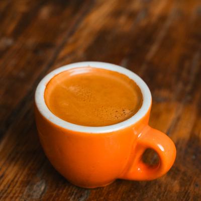 Shot of espresso served in a small, orange and white demitasse cup.