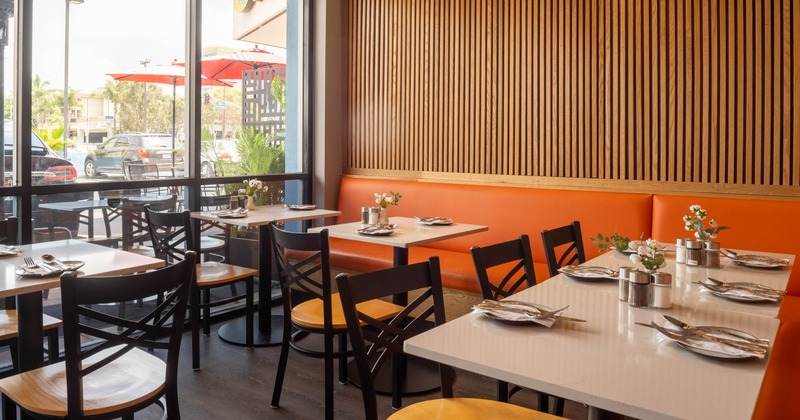 Interior of a restaurant with tables, chairs, and a large window with natural light