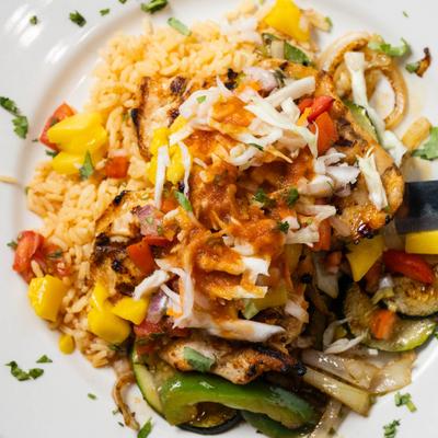 A plate of grilled chicken with rice, mango salsa, and grilled vegetables.