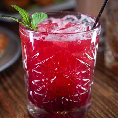 A blackberry smash cocktail with mint on a wooden table.