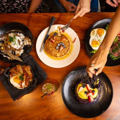 Top view of disshes served on the table with people taking bites of food.