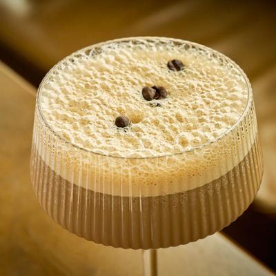 An espresso martini cocktail in a ribbed glass, garnished with coffee beans.