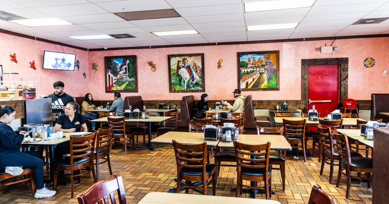 Interior of a restaurant with peach walls, decorative paintings, and wooden furnishings