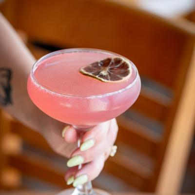 A hand holding The Cosmopolitan cocktail, garnished with a dry citrus slice.