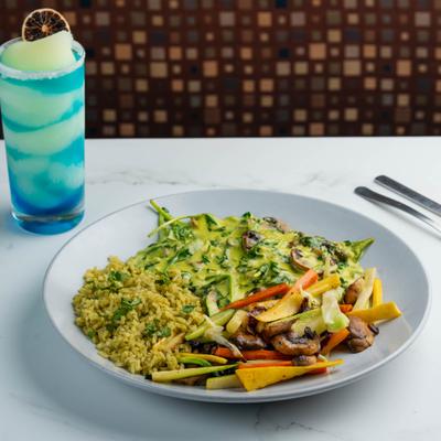Green rice with grilled vegetables and creamy green sauce served with a blue cocktail.