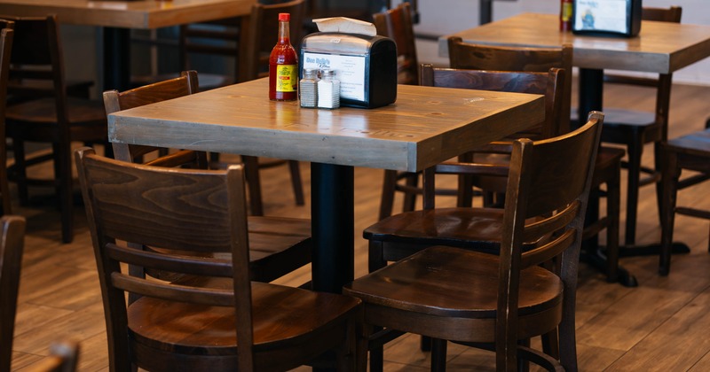 Interior of a dining area with wooden tables and chairs, featuring napkin dispensers