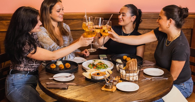 Indoors, a group of customers toasting with white sangria  at a table with served food