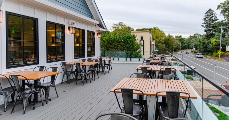 Outdoor dining area on a raised deck with tables and chairs beside a road