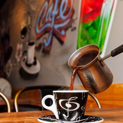 Turkish coffee being poured from a traditional coffee pot into a patterned cup.