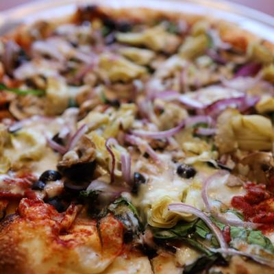 Pizza with artichoke hearts, spinach, mushrooms, tomatoes, olives, basil, and red onions.