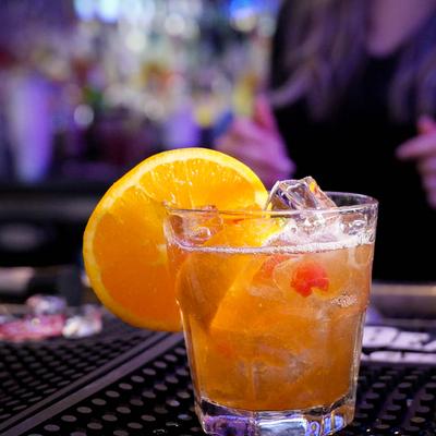 Old Fashioned cocktail with orange garnish, resting on a bar mat, close up.